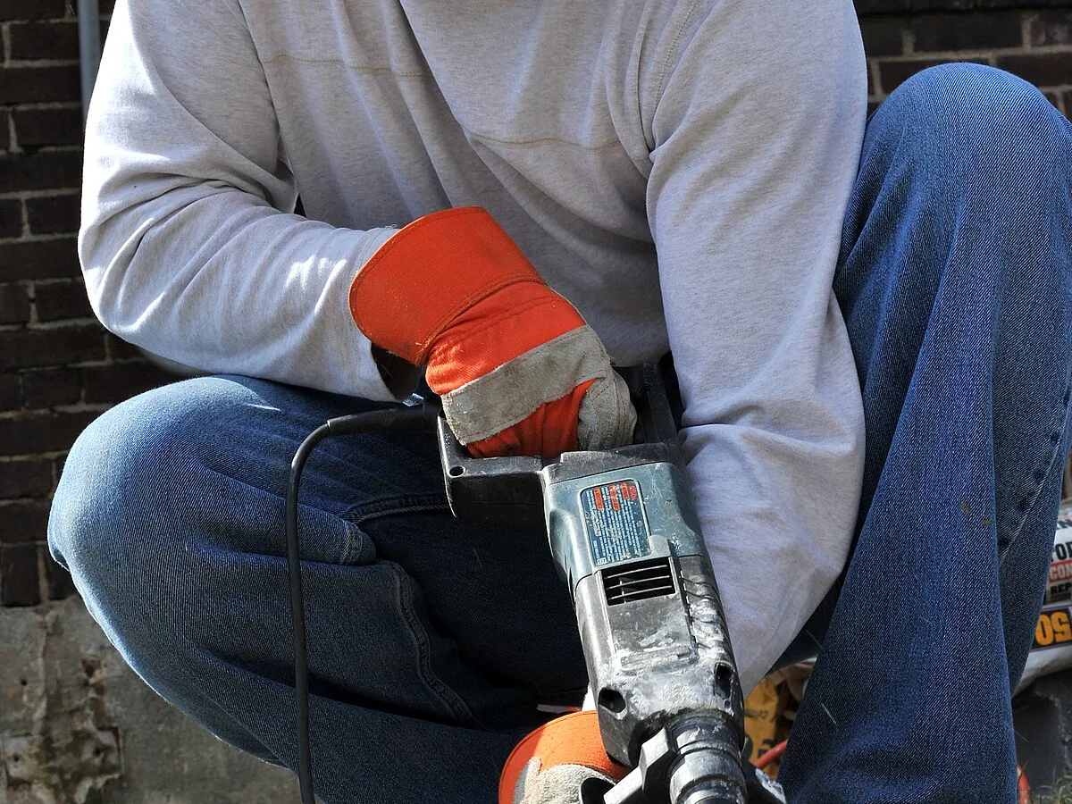 Craftsperson in safety glasses repairing a concrete walkway with a hammer drill